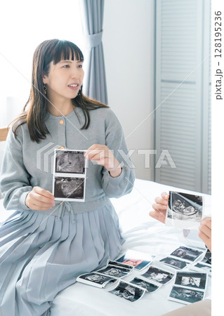 寝室でエコー写真を見ながら赤ちゃんが生まれてくるのを待ち望んでいる母と娘 128195236