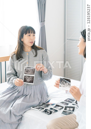 寝室でエコー写真を見ながら赤ちゃんが生まれてくるのを待ち望んでいる母と娘 寝室でエコー写真を見ながら赤ちゃんが生まれてくるのを待ち望んでいる母と娘 128195237