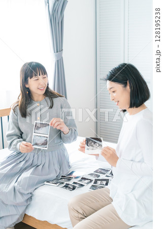 寝室でエコー写真を見ながら赤ちゃんが生まれてくるのを待ち望んでいる母と娘 128195238