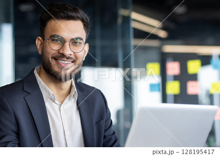 Mature man businessman sitting at a desk using a laptop, smiling confidently.This image beautifully captures the essence of productivity and professionalism 128195417