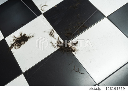 Clumps of hair scattered on a black and white tiled floor in a salon Clumps of hair scattered on a black and white tiled floor in a salon 128195859