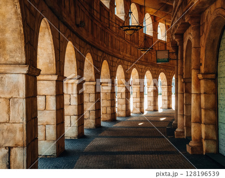 Sunlit Stone Archway In Macau: Elegant Curved Colonnade With Repeating Arches And Warm Shadows Evoking Classical Roman Architecture In A Historic-Style Setting 128196539