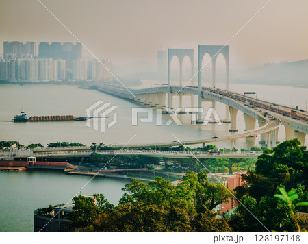 Macau Bridge Crossing Pearl River Estuary: Elegant White Arches Connecting City Districts Over Calm Waters With High-Rises In The Background On A Hazy Afternoon Macau Bridge Crossing Pearl River Estuary: Elegant White Arches Connecting City Districts Over Calm Waters With High-Rises In The Background On A Hazy Afternoon 128197148