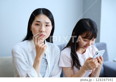 スマホに夢中になる娘を心配する母親のイメージ スマホに夢中になる娘を心配する母親のイメージ 128197541