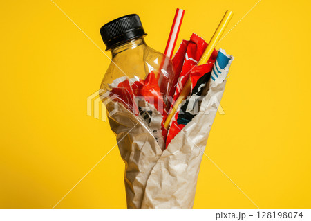 Crushed plastic bottle and colorful straws entangled with paper against vibrant yellow background symbolizes waste and recycling issues, AI Generative 128198074