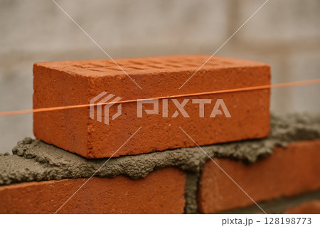 Red brick aligned by masonry string on a bed of mortar during precise bricklaying at a construction site, illustrating building techniques, AI Generative 128198773
