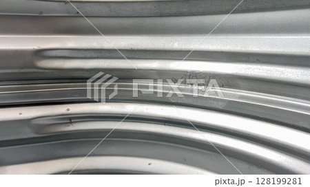 Detailed view of the metallic surface of a basement window well showing natural wear and texture. The lighting emphasizes curved ridges and material imperfections. Detailed view of the metallic surface of a basement window well showing natural wear and texture. The lighting emphasizes curved ridges and material imperfections. 128199281