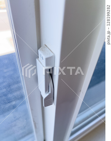 Close-up of a white window lock on a sliding window frame. The clean surface and simple mechanism are visible under natural daylight. Close-up of a white window lock on a sliding window frame. The clean surface and simple mechanism are visible under natural daylight. 128199282
