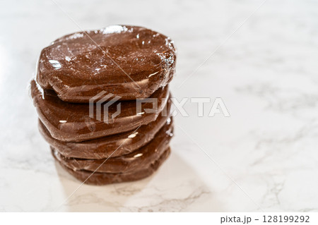 Multiple discs of Chocolate Gingerbread Cookie Dough wrapped in plastic wrap, stacked and ready to chill. These dough discs make it convenient to shape cookies for holiday baking. 128199292