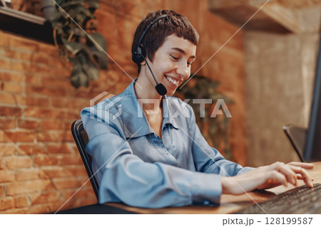 A dedicated professional woman wearing a headset is actively engaged in her work at the desk 128199587