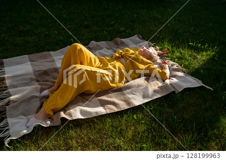 A serene scene of a woman dressed in yellow, leisurely relaxing on a blanket in nature, enjoying 128199963