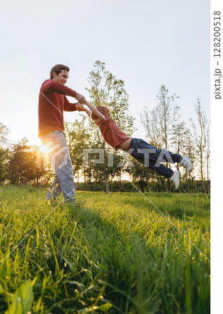 Father spinning son in park at sunset Father spinning son in park at sunset 128200518