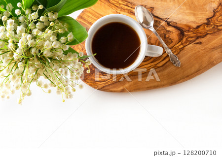 Cup of coffee and fresh bouquet of blooming lily of valley flowers on wooden stand on white background. Top view, flat lay, copy space. 128200710