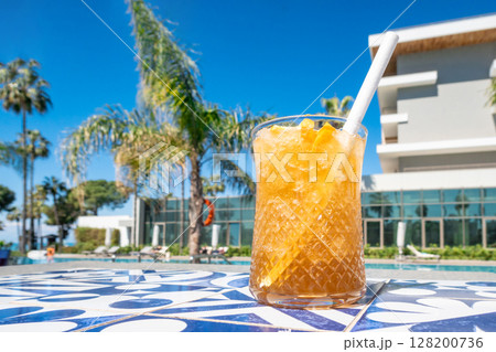 Fresh alcoholic cocktail with ice in glass on swimming pool. Hard strong drink on sunlight with palms. Concept summer luxury holiday and travel Fresh alcoholic cocktail with ice in glass on swimming pool. Hard strong drink on sunlight with palms. Concept summer luxury holiday and travel 128200736