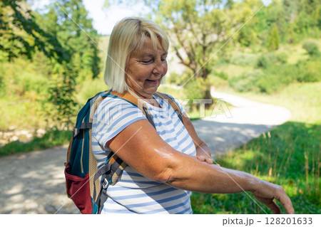 Senior Woman Applying Cream or Repellent During Hike 128201633
