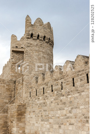 Ancient stone fortress walls featuring a textured round tower under a blue sky Ancient stone fortress walls featuring a textured round tower under a blue sky 128202525
