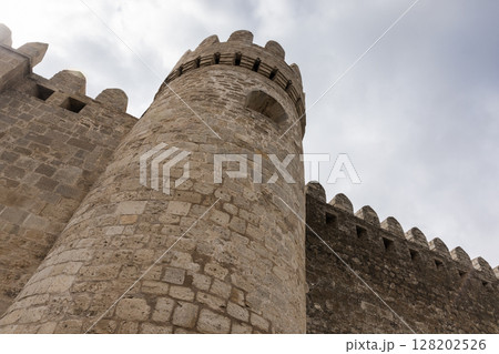 Ancient stone fortress featuring round tower under cloudy sky 128202526