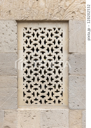 Intricately carved stonework featuring a geometric perforated window design 128202532
