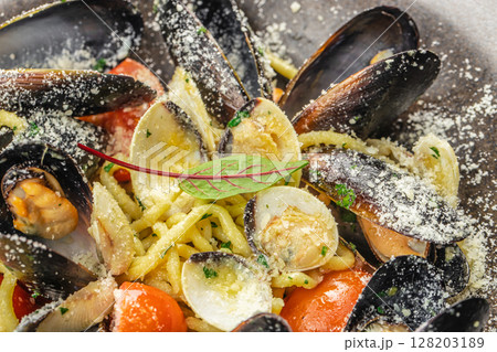 A close-up of gourmet seafood pasta with mussels, clams, cherry tomatoes, parmesan cheese, and fresh herbs, showcasing vibrant colors and rich textures 128203189