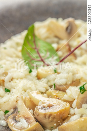A close-up of creamy mushroom risotto with tender sauteed mushrooms, parmesan cheese, and fresh herbs, beautifully garnished with a vibrant microgreen leaf 128203343