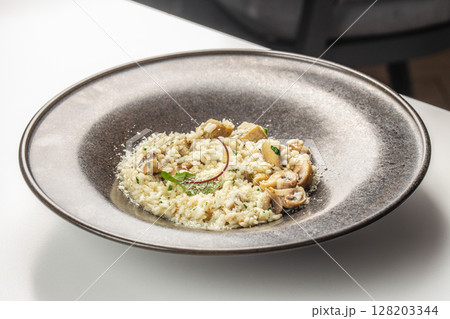A creamy mushroom risotto garnished with parmesan cheese, fresh herbs, and sauteed mushrooms, elegantly served on a dark ceramic plate 128203344