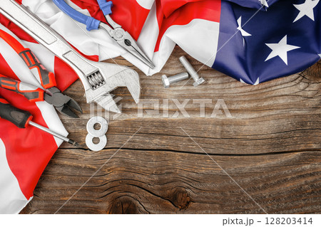 American flag draped with hand tools and bolts on rustic wood, honoring Labor Day and the hardworking spirit of the nation 128203414