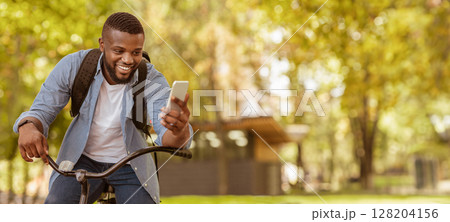Video Call. Happy African American Guy Riding Bicycle Outdoors And Chatting With Friends Online On Smartphone 128204156