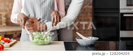 Cooking together. Black man hugging woman while she is mixing healthy salad, cropped Cooking together. Black man hugging woman while she is mixing healthy salad, cropped 128204203
