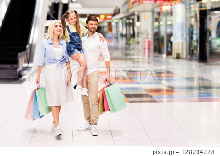 A family of three, a man, a woman, and a young girl, are walking through a modern shopping mall. They are carrying colorful shopping bags and smiling, copy space A family of three, a man, a woman, and a young girl, are walking through a modern shopping mall. They are carrying colorful shopping bags and smiling, copy space 128204228