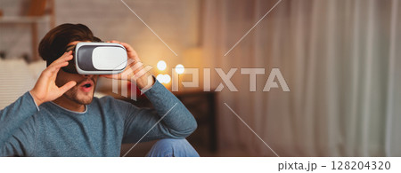 Virtual Reality. Young Man Using VR Headset Playing Videogame Indoor In The Evening. Selective Focus Virtual Reality. Young Man Using VR Headset Playing Videogame Indoor In The Evening. Selective Focus 128204320