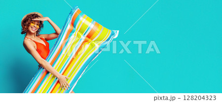 Beautiful African American woman in swimsuit, sunglasses and summer hat holding inflatable raft, isolated on blue background, panorama with copy space Beautiful African American woman in swimsuit, sunglasses and summer hat holding inflatable raft, isolated on blue background, panorama with copy space 128204323