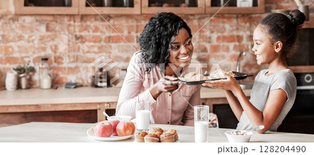 Happy little african girl showing self made croissants to her cheerful mom, kitchen interior 128204490