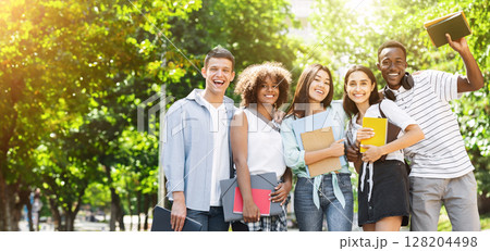 Group of multicultural university students posing outdoors after study, sincerely smiling at camera, standing in park, free space Group of multicultural university students posing outdoors after study, sincerely smiling at camera, standing in park, free space 128204498