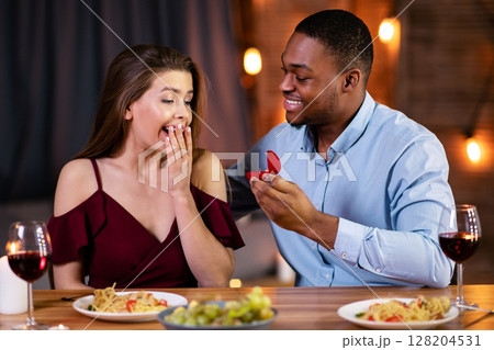 Marriage Proposal. Romantic Black Boyfriend Proposing Girlfriend To Marry Him On Dinner Date In Restaurant, Presenting Diamond Ring. Elegant Multiracial Couple Celebrating Valentines Day Together Marriage Proposal. Romantic Black Boyfriend Proposing Girlfriend To Marry Him On Dinner Date In Restaurant, Presenting Diamond Ring. Elegant Multiracial Couple Celebrating Valentines Day Together 128204531