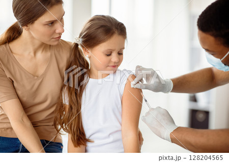 Doctor doing injection of covid-19 vaccine to little patient at clinic. Cute girl with her mom on visit to physician, being immunized against coronavirus. Medicine, vaccination and healthcare concept Doctor doing injection of covid-19 vaccine to little patient at clinic. Cute girl with her mom on visit to physician, being immunized against coronavirus. Medicine, vaccination and healthcare concept 128204565