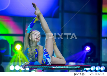 Plastic little girl gymnast. A child with a flexible body performs on stage. 128204704