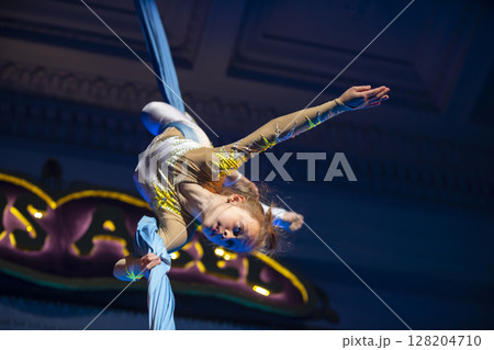 The girl performs acrobatic numbers on the canvases. A small circus artist performs on the canvases of acrobats. Child perform acrobatic elements in the air 128204710