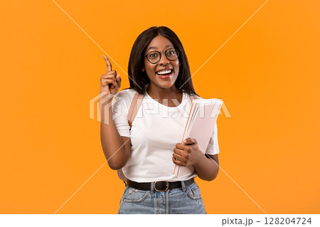 Inspired young black woman student in white t-shirt with backpack and books raising finger up and smiling, wearing glasses, having creative idea, orange studio background, copy space Inspired young black woman student in white t-shirt with backpack and books raising finger up and smiling, wearing glasses, having creative idea, orange studio background, copy space 128204724