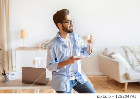 Handsome Eastern Man Relaxing With Cup Of Coffee After Working At Home Office, Smiling Millennial Arab Freelancer Guy Leaning Desk With Laptop, Enjoying Remote Work Opportunities, Copy Space Handsome Eastern Man Relaxing With Cup Of Coffee After Working At Home Office, Smiling Millennial Arab Freelancer Guy Leaning Desk With Laptop, Enjoying Remote Work Opportunities, Copy Space 128204743