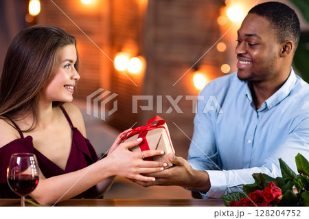 Loving Black Boyfriend Giving Romantic Gift To His White Girfriend In Restaurant, Greeting With Holiday, Young Multiracial Couple Celebrating Valentine's Or International Women's Day Together Loving Black Boyfriend Giving Romantic Gift To His White Girfriend In Restaurant, Greeting With Holiday, Young Multiracial Couple Celebrating Valentine's Or International Women's Day Together 128204752