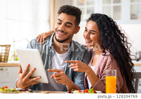 Cheerful Middle Eastern Spouses Using Digital Tablet While Having Breakfast In Kitchen At Home, Happy Young Arab Couple Shopping Online Or Checking Social Networks While Having Tasty Meal, Free Space Cheerful Middle Eastern Spouses Using Digital Tablet While Having Breakfast In Kitchen At Home, Happy Young Arab Couple Shopping Online Or Checking Social Networks While Having Tasty Meal, Free Space 128204769