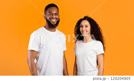 Multiethnic Couple Posing Wearing White T-Shirts Smiling To Camera Standing Over Yellow Studio Background. Diverse Friendship And Relationship. Happy Multiracial Young Family's Portrait. Panorama Multiethnic Couple Posing Wearing White T-Shirts Smiling To Camera Standing Over Yellow Studio Background. Diverse Friendship And Relationship. Happy Multiracial Young Family's Portrait. Panorama 128204805