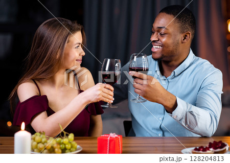 Affectionate Mixed Couple Having Romantic Dinner In Restaurant, Drinking Red Wine And Smiling. Young Interracial Lovers Celebrating Anniversary Or Valentine's Day Together In Elegant Atmosphere 128204813