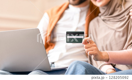 Online Shopping. Muslim Couple Using Credit Card And Laptop Computer Buying Things In Internet Shop Sitting On Sofa At Home. Sales And Discounts Concept. Selective Focus, Shallow Depth, Cropped Online Shopping. Muslim Couple Using Credit Card And Laptop Computer Buying Things In Internet Shop Sitting On Sofa At Home. Sales And Discounts Concept. Selective Focus, Shallow Depth, Cropped 128205092