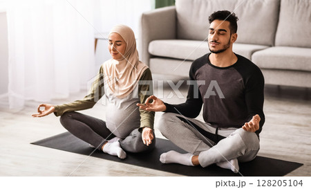 Pregnant Muslim Woman In Hijab Practicing Yoga With Her Husband At Home, Expecting Middle Eastern Spouses Meditating Together On Mat In Living Room, Sitting In Lotus Pose With Closed Eyes, Free Space Pregnant Muslim Woman In Hijab Practicing Yoga With Her Husband At Home, Expecting Middle Eastern Spouses Meditating Together On Mat In Living Room, Sitting In Lotus Pose With Closed Eyes, Free Space 128205104