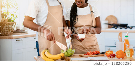Young Happy African American Lovers In Aprons Cooking Together In Kitchen, Cheerful Black Couple Enjoying Preparing Healthy Food At Home, Adding Seasoning To Fresh Vegetable Salad, Free Space 128205280