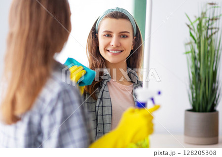 Cheerful millennial housewife wiping mirror with rag, using spray detergent to clean looking glass at home. Young woman doing domestic chores, keeping her apartment tidy Cheerful millennial housewife wiping mirror with rag, using spray detergent to clean looking glass at home. Young woman doing domestic chores, keeping her apartment tidy 128205308
