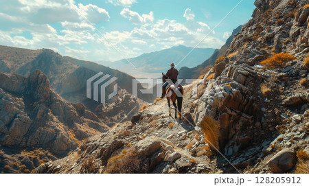 A rider explorers a rocky mountain trail on horseback, surrounded by stunning natural scenery and blue skies. 128205912