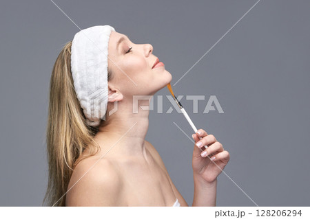 Young caucasian female applying face mask with brush in skincare routine 128206294