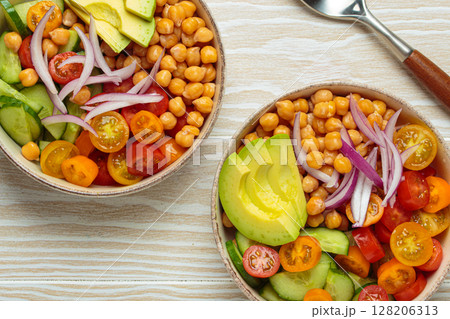 Two bowls with vibrant vegetarian chickpea salad with fresh vegetables in ceramic bowls top view 128206313